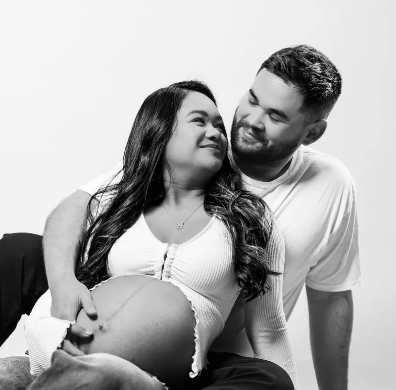 Black and white studio portrait of an expecting couple smiling at each other