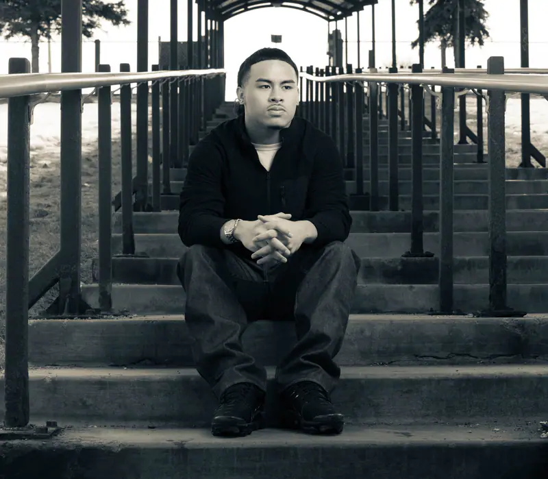 Toned senior portrait of a young man sitting on stadium steps, hands clasped